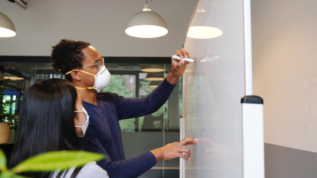 Procurement professionals wearing masks collaborate on a white board